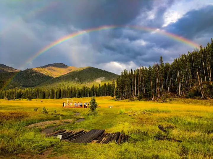 A rainbow over the green meadow below Galena’s forested ridges
